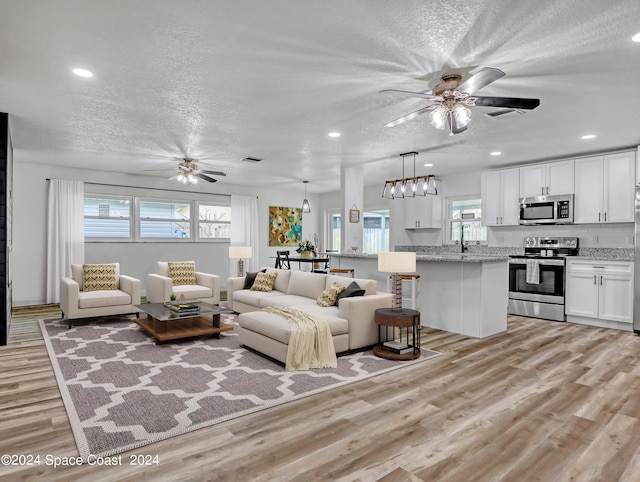 living room with ceiling fan, light hardwood / wood-style flooring, a healthy amount of sunlight, and a textured ceiling