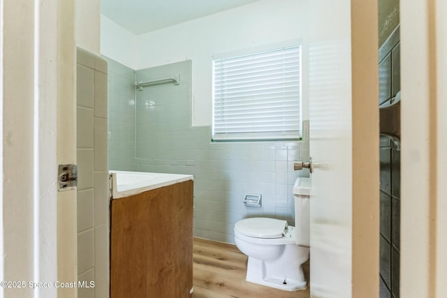 bathroom featuring vanity, toilet, wood-type flooring, and tile walls