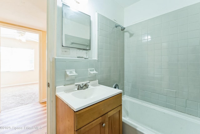 bathroom featuring hardwood / wood-style floors, vanity, backsplash, tiled shower / bath combo, and tile walls