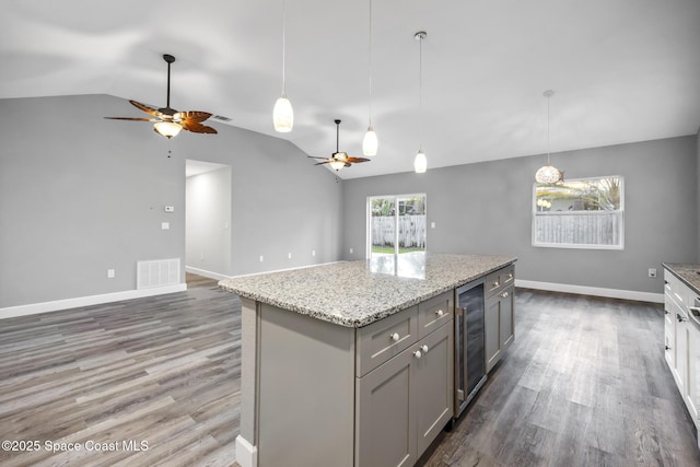 kitchen with gray cabinetry, decorative light fixtures, a kitchen island, and vaulted ceiling