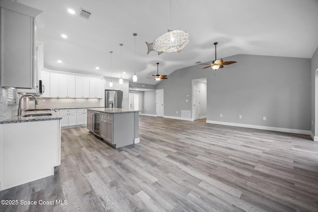 kitchen with stainless steel refrigerator with ice dispenser, decorative light fixtures, white cabinets, a center island, and lofted ceiling