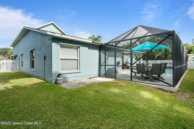 rear view of house featuring a lawn, glass enclosure, and a patio