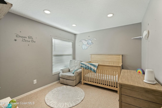 carpeted bedroom featuring a textured ceiling and a nursery area