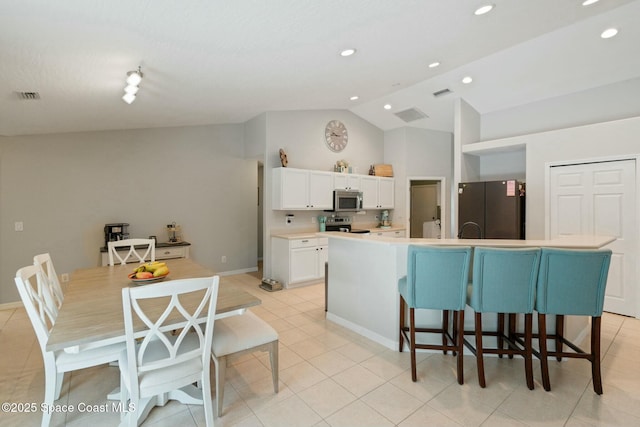 kitchen with white cabinetry, a kitchen breakfast bar, lofted ceiling, a center island with sink, and appliances with stainless steel finishes