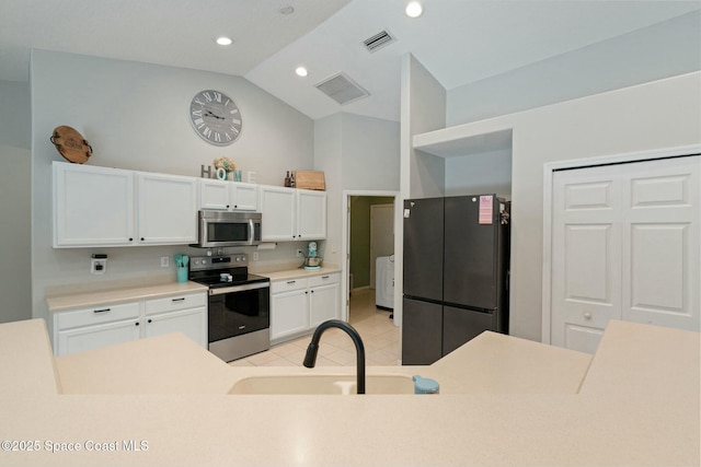 kitchen featuring stainless steel appliances, vaulted ceiling, sink, white cabinets, and washer / clothes dryer