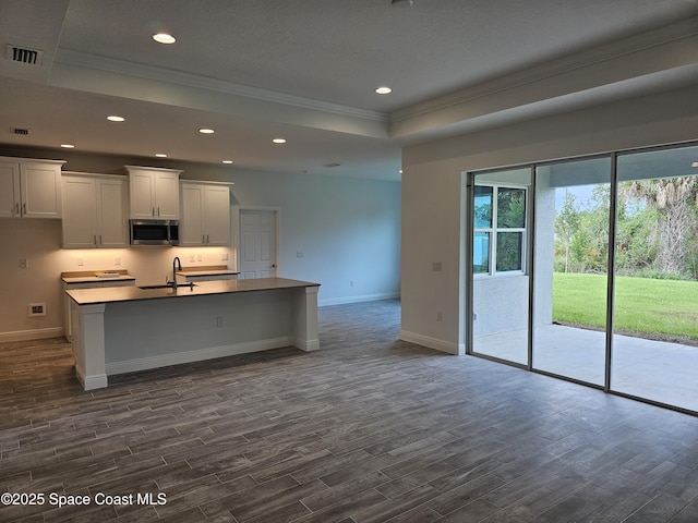 kitchen with dark wood-type flooring, a tray ceiling, a center island with sink, and sink