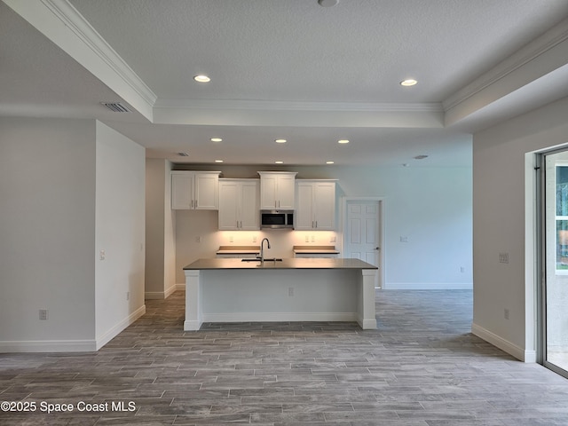 kitchen featuring white cabinets, an island with sink, sink, a tray ceiling, and light hardwood / wood-style flooring