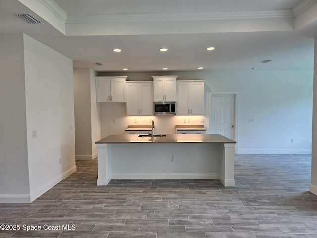 kitchen featuring white cabinets, sink, ornamental molding, a kitchen island with sink, and light wood-type flooring