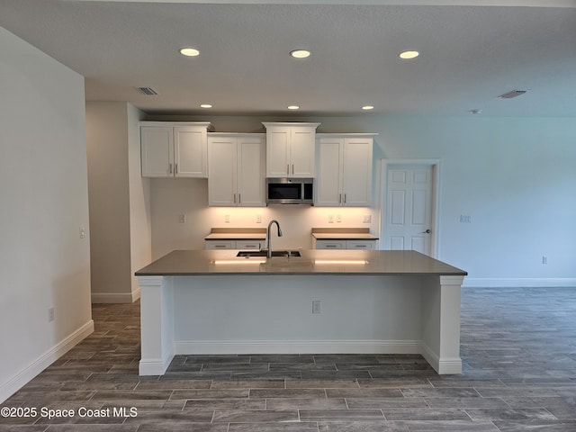 kitchen featuring a kitchen island with sink, dark hardwood / wood-style flooring, sink, and white cabinetry