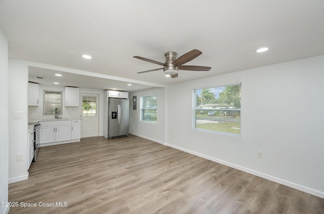 unfurnished living room featuring a textured ceiling, light hardwood / wood-style flooring, ceiling fan, and sink