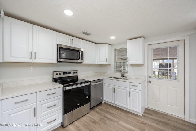 kitchen with white cabinets, sink, a textured ceiling, appliances with stainless steel finishes, and light hardwood / wood-style floors