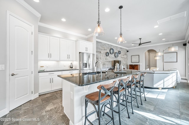 kitchen featuring white cabinets, a kitchen breakfast bar, ceiling fan, stainless steel fridge, and an island with sink