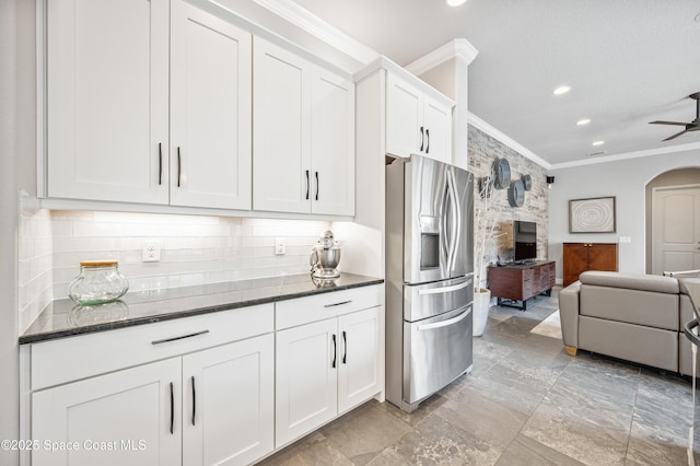 kitchen featuring stainless steel fridge, tasteful backsplash, dark stone counters, crown molding, and white cabinets