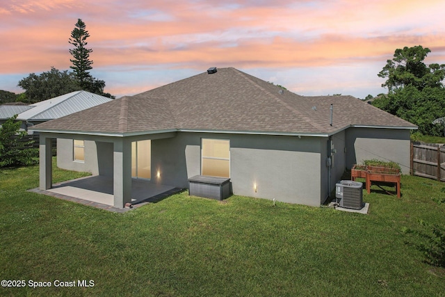 back house at dusk featuring a lawn, central air condition unit, and a patio