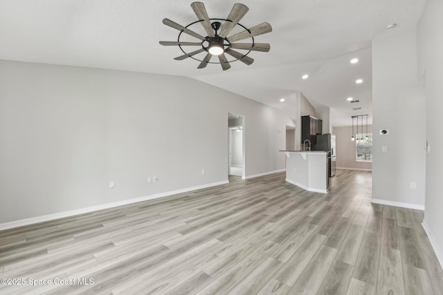 unfurnished living room featuring ceiling fan, lofted ceiling, sink, and light hardwood / wood-style flooring