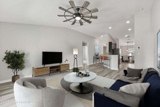 living room featuring ceiling fan, sink, light hardwood / wood-style flooring, and vaulted ceiling