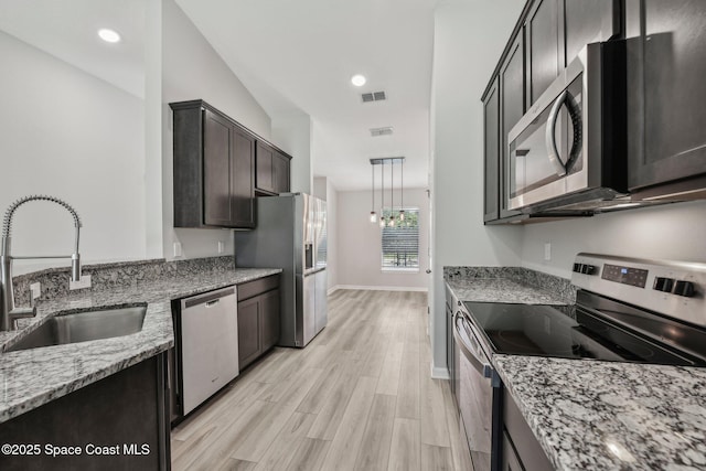 kitchen with dark brown cabinetry, light stone countertops, sink, stainless steel appliances, and light hardwood / wood-style floors