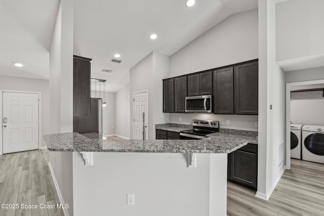 kitchen featuring kitchen peninsula, light stone counters, a breakfast bar, stainless steel appliances, and independent washer and dryer