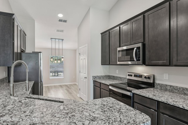 kitchen with light stone countertops, appliances with stainless steel finishes, dark brown cabinetry, and decorative light fixtures