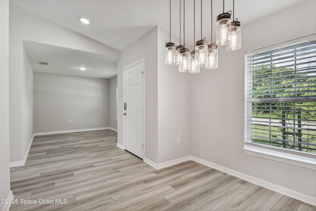 empty room featuring a chandelier, plenty of natural light, light hardwood / wood-style floors, and vaulted ceiling