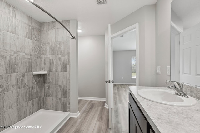 bathroom with hardwood / wood-style floors, vanity, and tiled shower