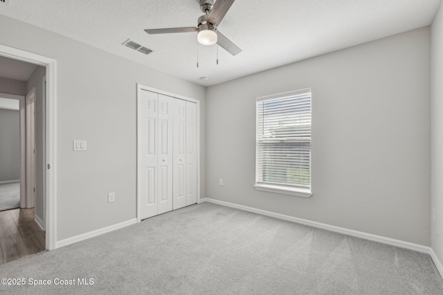 unfurnished bedroom featuring light carpet, a textured ceiling, a closet, and ceiling fan