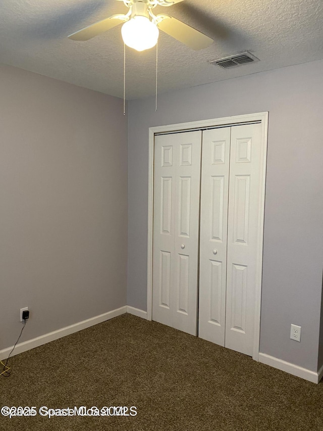 unfurnished bedroom with dark colored carpet, ceiling fan, a textured ceiling, and a closet