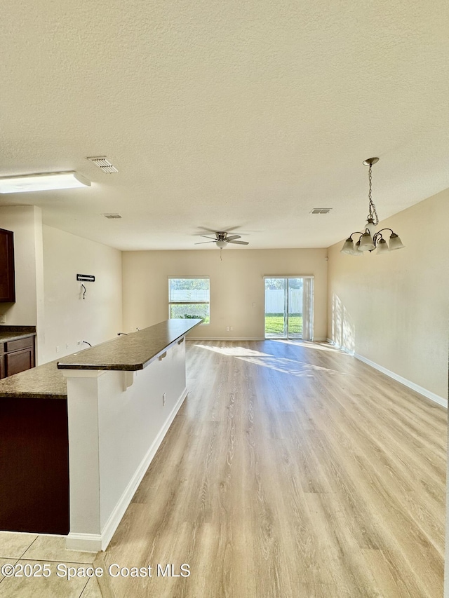 interior space with light hardwood / wood-style flooring, ceiling fan with notable chandelier, and a textured ceiling