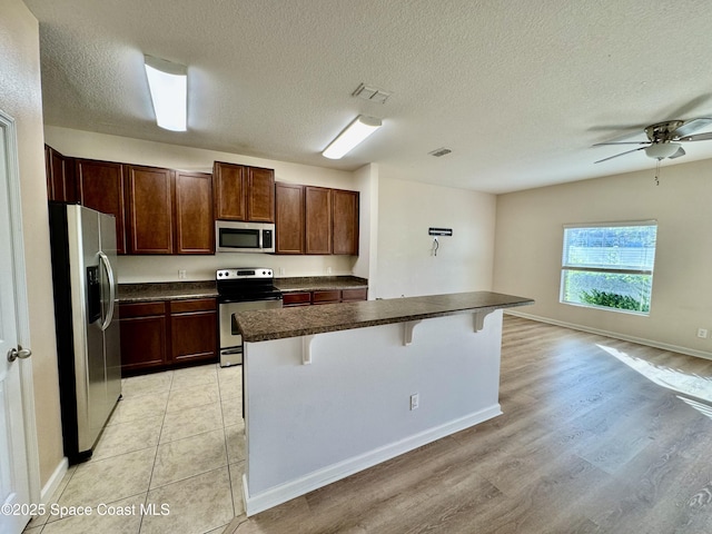 kitchen with a kitchen breakfast bar, a textured ceiling, stainless steel appliances, ceiling fan, and a center island with sink