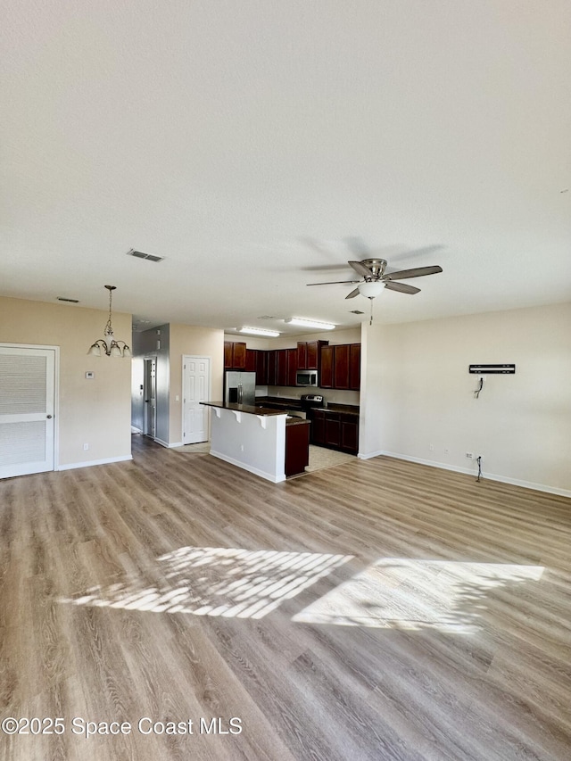 unfurnished living room with ceiling fan with notable chandelier, light hardwood / wood-style floors, and a textured ceiling