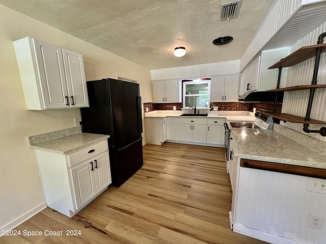 kitchen with black refrigerator, electric range oven, white cabinets, and sink