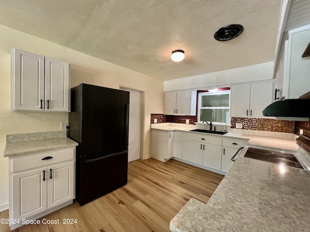 kitchen featuring black fridge, white cabinetry, sink, and stove