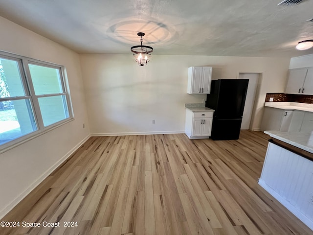 kitchen featuring black refrigerator, pendant lighting, light hardwood / wood-style flooring, a notable chandelier, and white cabinetry