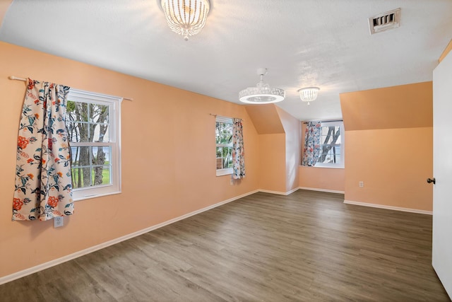 bonus room featuring plenty of natural light, dark hardwood / wood-style floors, and a notable chandelier