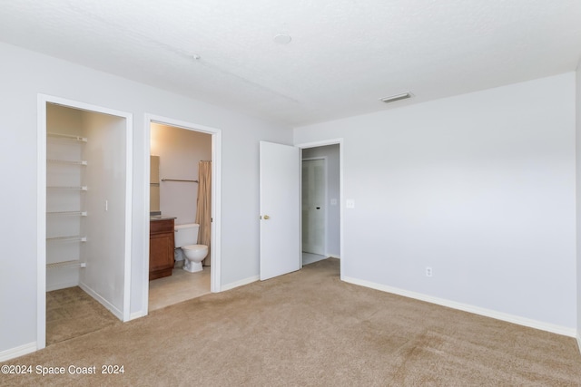 unfurnished bedroom featuring a walk in closet, light colored carpet, ensuite bath, and a closet