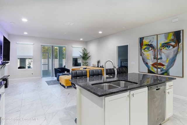 kitchen featuring white cabinets, dishwasher, a kitchen island with sink, dark stone countertops, and sink