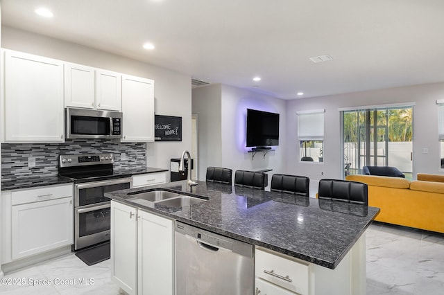 kitchen with an island with sink, white cabinetry, appliances with stainless steel finishes, dark stone countertops, and sink