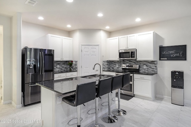 kitchen with sink, white cabinets, an island with sink, dark stone counters, and appliances with stainless steel finishes