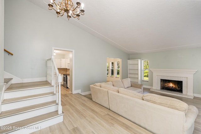 living room with an inviting chandelier, light hardwood / wood-style floors, high vaulted ceiling, and a brick fireplace