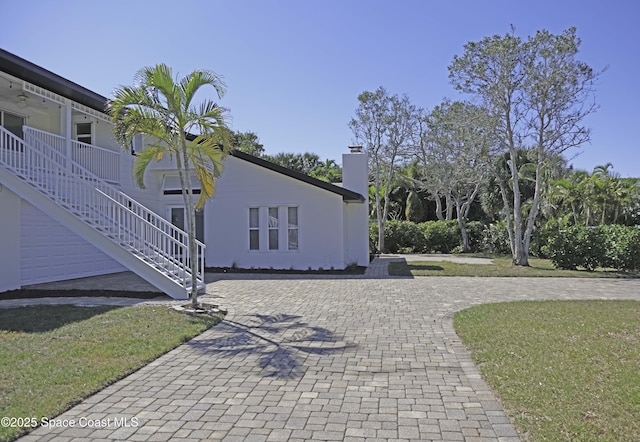 view of home's exterior featuring stairway, stucco siding, a chimney, a yard, and driveway