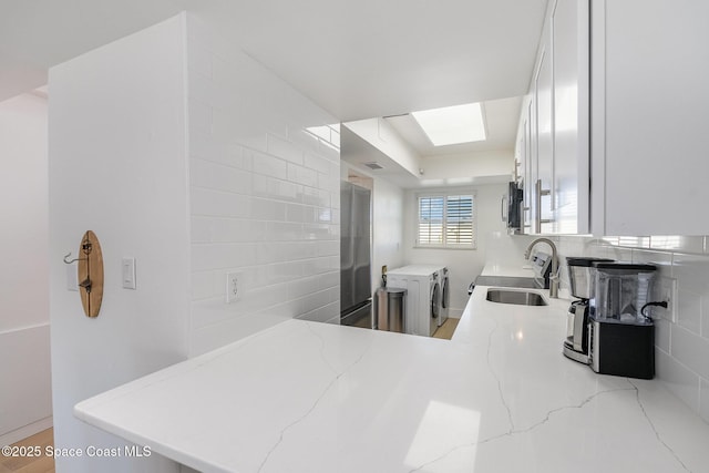 kitchen with white cabinets, light stone countertops, kitchen peninsula, and sink