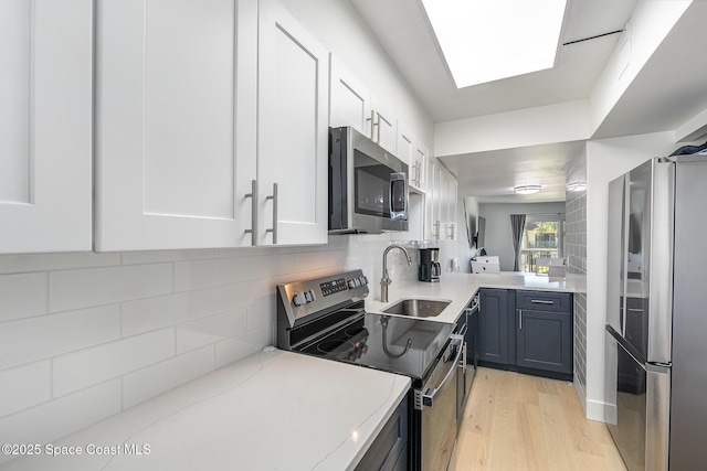 kitchen featuring sink, stainless steel appliances, light hardwood / wood-style floors, decorative backsplash, and white cabinets