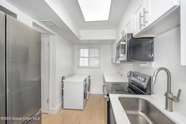 kitchen with white cabinetry, sink, stainless steel appliances, independent washer and dryer, and decorative backsplash