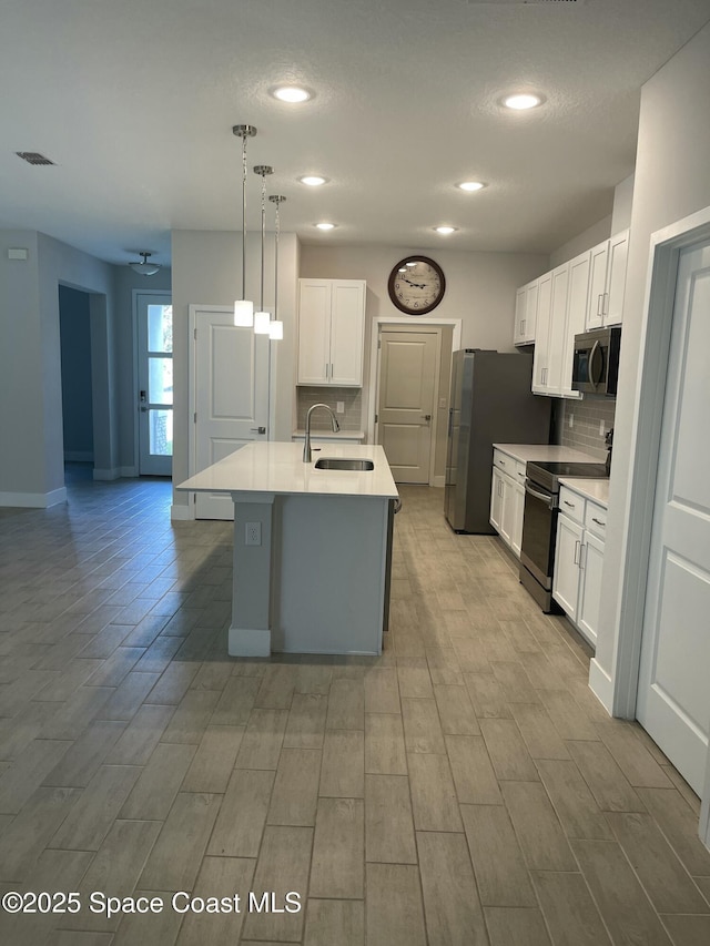 kitchen with sink, a center island with sink, hanging light fixtures, stainless steel appliances, and white cabinets