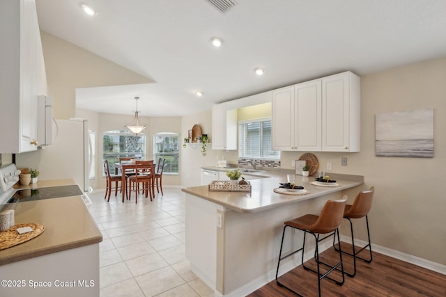 kitchen featuring kitchen peninsula, a kitchen breakfast bar, pendant lighting, white cabinets, and range