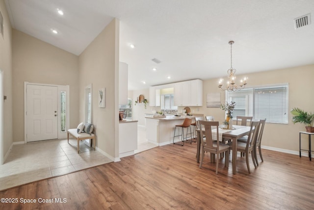 dining room featuring light wood-type flooring, high vaulted ceiling, and an inviting chandelier