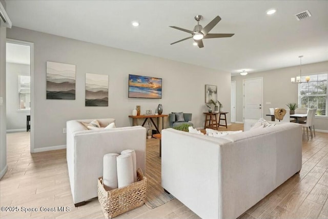 living room featuring ceiling fan with notable chandelier and light wood-type flooring