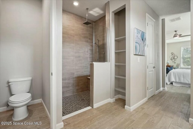 bathroom with ceiling fan, toilet, wood-type flooring, and tiled shower