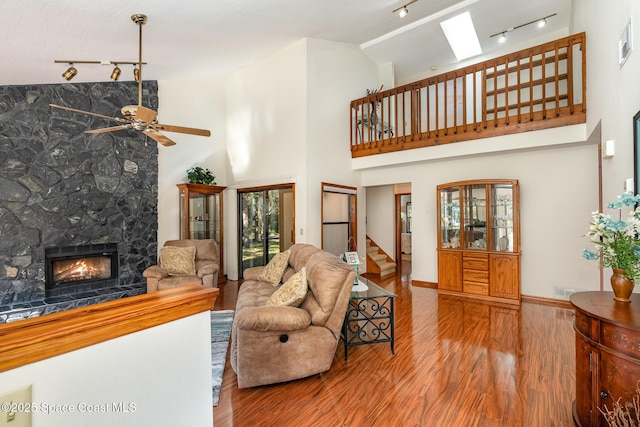 living room featuring a skylight, ceiling fan, a high ceiling, a stone fireplace, and hardwood / wood-style flooring