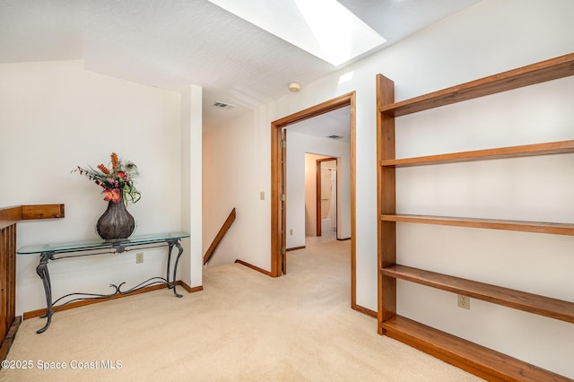 hallway featuring light carpet and lofted ceiling with skylight